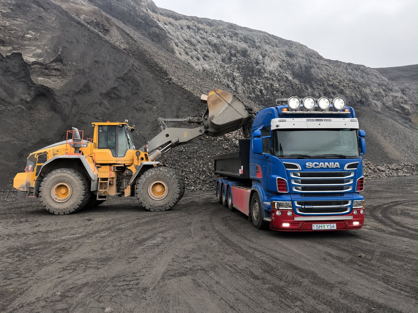 Volvo hjólaskófla mokar möl á Scania vörubíl í íslenskri námu